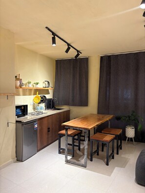A compact kitchen with a dining area, including a wooden table and chairs, a dishwasher, and a small refrigerator. - Canguu Bali Apartment Exora Spark  (Cairo Governorate)