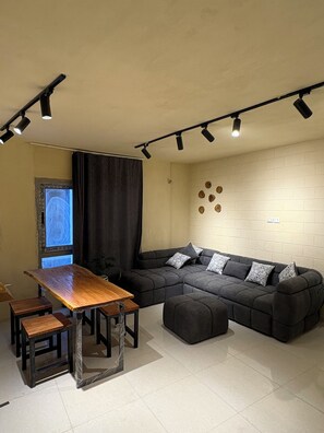 A modern living space with a sectional sofa, a wooden dining table, and a black couch. - Canguu Bali Apartment Exora Spark  (Cairo Governorate)