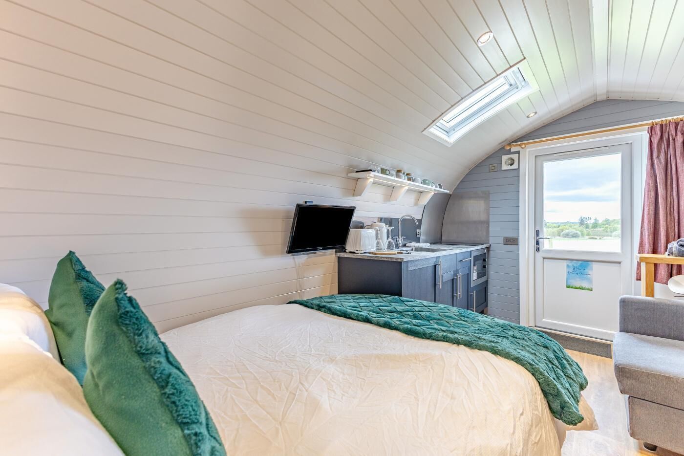 A bedroom with a bed, a television, a kitchenette, and a balcony with curtains.