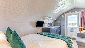 A bedroom with a bed, a television, a kitchenette, and a balcony with curtains.