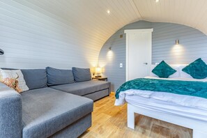 A cozy room with a grey sofa, a bed with teal pillows, a nightstand, and a lamp.