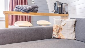 A modern living room with a grey sofa, a wooden shelf with folded towels, a coffee machine, and a wall-mounted thermostat. - 1 Bed in Forfar (oc-t34622) (Forfar)