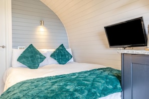A bedroom with a bed, a television on a stand, and a wall-mounted light fixture.