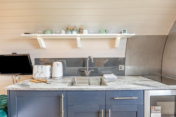 A modern kitchen with a marble countertop, stainless steel sink, and a flat-screen TV.