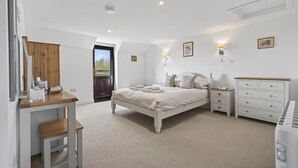 A bedroom with a bed, bedside tables, a dresser, a desk, and a chair. There is a door leading to an outdoor area. - 1 Bed in Milton Abbas (oc-v35014) (Milton Abbas)