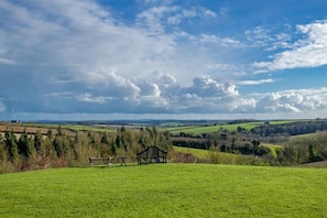 Ein grünes Feld mit einer Bank und einem Tisch, mit Blick auf eine ländliche Landschaft aus Feldern und Bäumen.