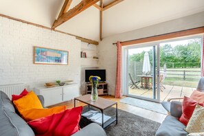 Ein Wohnzimmer mit einer Couch, einem Couchtisch, einem Fernseher und Blick ins Freie durch eine Glastür.