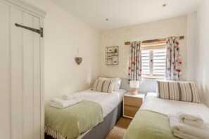 Ein Schlafzimmer mit zwei Betten, einem Nachttisch mit Lampe, einer herzförmigen Dekoration und einem Fenster mit Vorhängen.