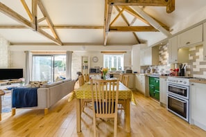 A spacious living area with a dining table, sofa, and kitchen with wooden beams and a green stove. - 3 Bed in Cranmer (oc-s45787) (Cranmer)