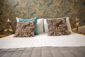 A bed with patterned pillows, a plain wall, and a nightstand with a lamp and a glass of water. - 2 Bed in Cranmer (oc-t45788) (Cranmer)
