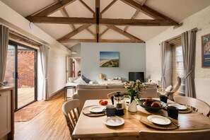 A dining area with a wooden table set for a meal, a sofa in the background, and a view of the outdoors through a glass door. - 2 Bed in Cranmer (oc-o45790) (Cranmer)