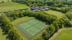 Oversigtsbillede af et boligområde med tennisbane og flere huse omgivet af grønt.