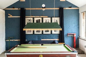 Ein Billardtisch in einem Raum mit blauer Ziegelwand, gerahmten Bildern und grüner Decke.