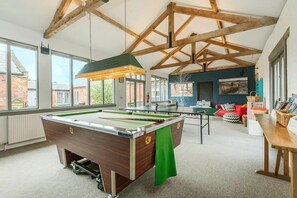 Une table de billard dans une pièce dotée d’un haut plafond, de grandes fenêtres et d’un coin salon confortable.