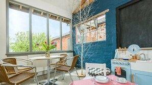 A dining area with a table set for two, a window with a view of trees, and a blue brick wall. - 2 Bed in Cranmer (oc-w45791) (Cranmer)