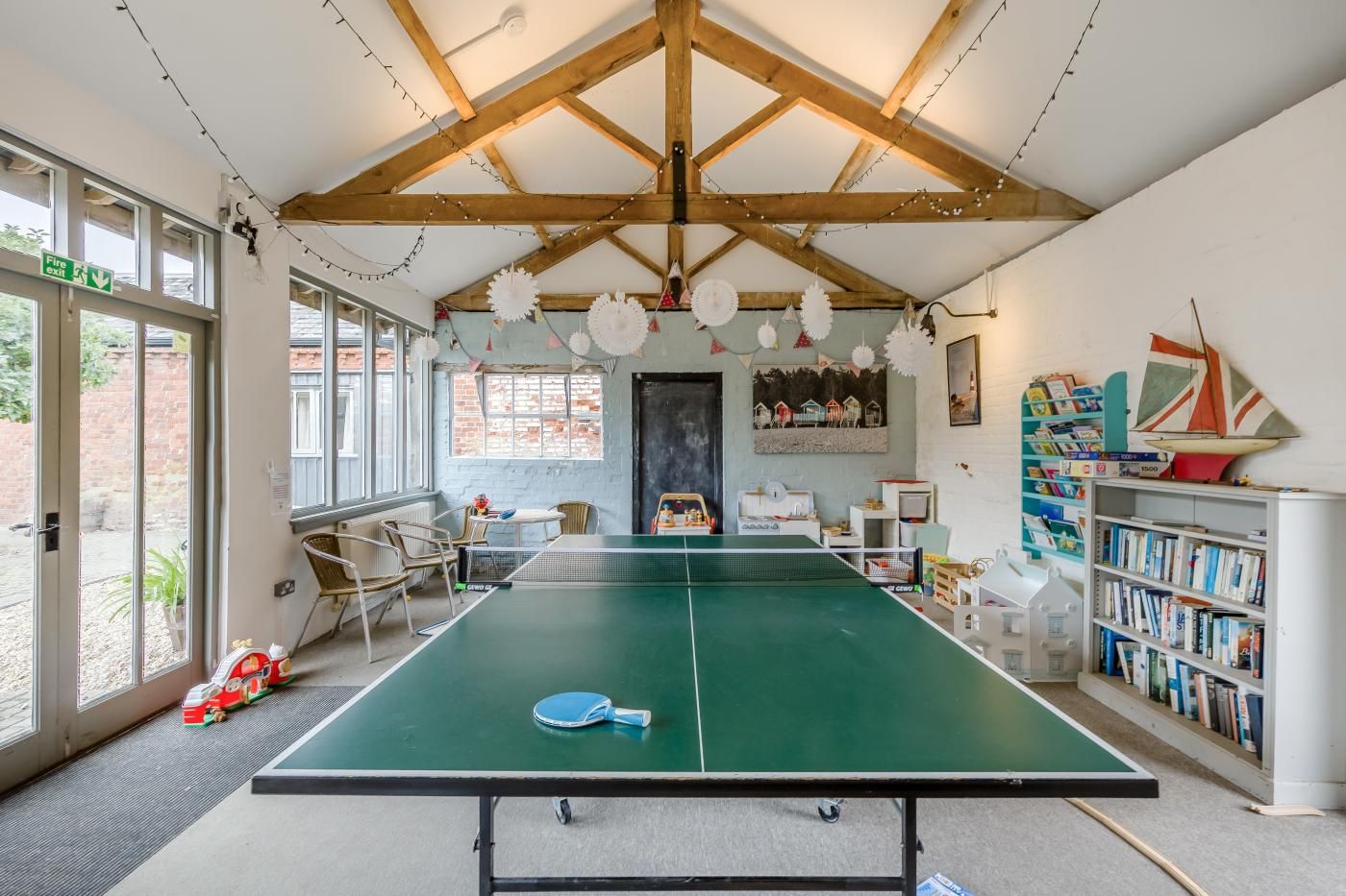 A room with a ping pong table, chairs, a bookshelf, and a door marked 'Fire exit'.