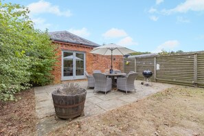 Eine Terrasse mit Tisch und Stühlen, einem Grill und einem Holzfass.
