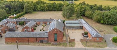 A large, open building with multiple brick structures, surrounded by green fields and trees.