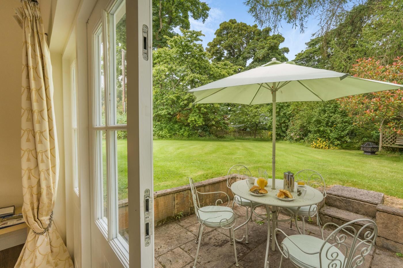 An open door leading to a patio with a table, chairs, and an umbrella.