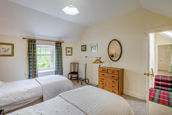 Een slaapkamer met twee enkele bedden, een dressoir, een stoel, een radiator en een raam met gordijnen.