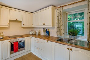 A kitchen with white cabinetry, a wooden countertop, a stove, a sink, and a window with a view of greenery. - 2 Bed in Newtyle (oc-b45543) (Newtyle)