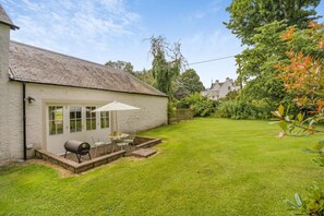 Een huis met een witte gevel, een terras met tuinmeubilair en een verzorgd gazon.