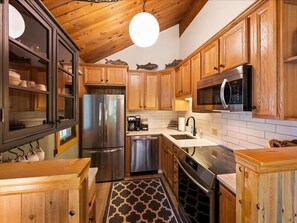 A kitchen with wooden cabinets, stainless steel appliances, and a patterned floor. - Escape to Ptarmigan Village 36 (Whitefish)