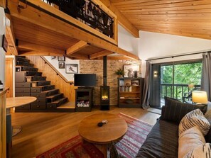 A wooden interior with a fireplace, a sofa, a TV, and a staircase. - Escape to Ptarmigan Village 36 (Whitefish)