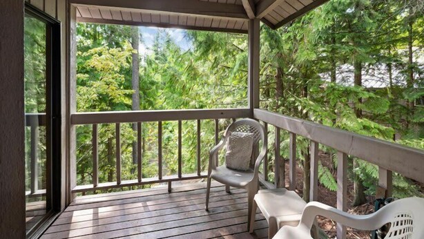 Eine überdachte Veranda mit Holzterrasse, einem Stuhl und Blick auf einen Wald.