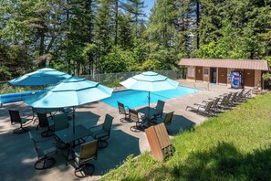 A pool area with umbrellas, lounge chairs, and a small building with a vending machine. - Escape to Ptarmigan Village 36 (Whitefish)