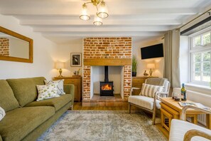 A cozy living room with a brick fireplace, a green sofa, a wooden coffee table, and a television mounted on the wall. - 2 Bed in Great Massingham (oc-a45882) (Great Massingham)