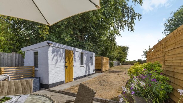 A small white building with a wooden door, a wooden bench, and a table with a glass. - 2 Bed in Great Massingham (oc-a45882) (Great Massingham)