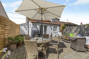 Eine Terrasse mit Korbmöbeln, einem Tisch und einem großen Sonnenschirm.