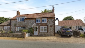 A two-story stone house with a tiled roof, a front door, and a driveway with two cars parked. - 2 Bed in Great Massingham (oc-a45882) (Great Massingham)