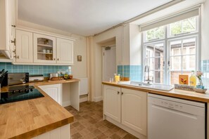 A kitchen with white cabinets, a wooden countertop, a dishwasher, and a window with a view of the outside. - 2 Bed in Higher Eype (oc-d45830) (Eype)