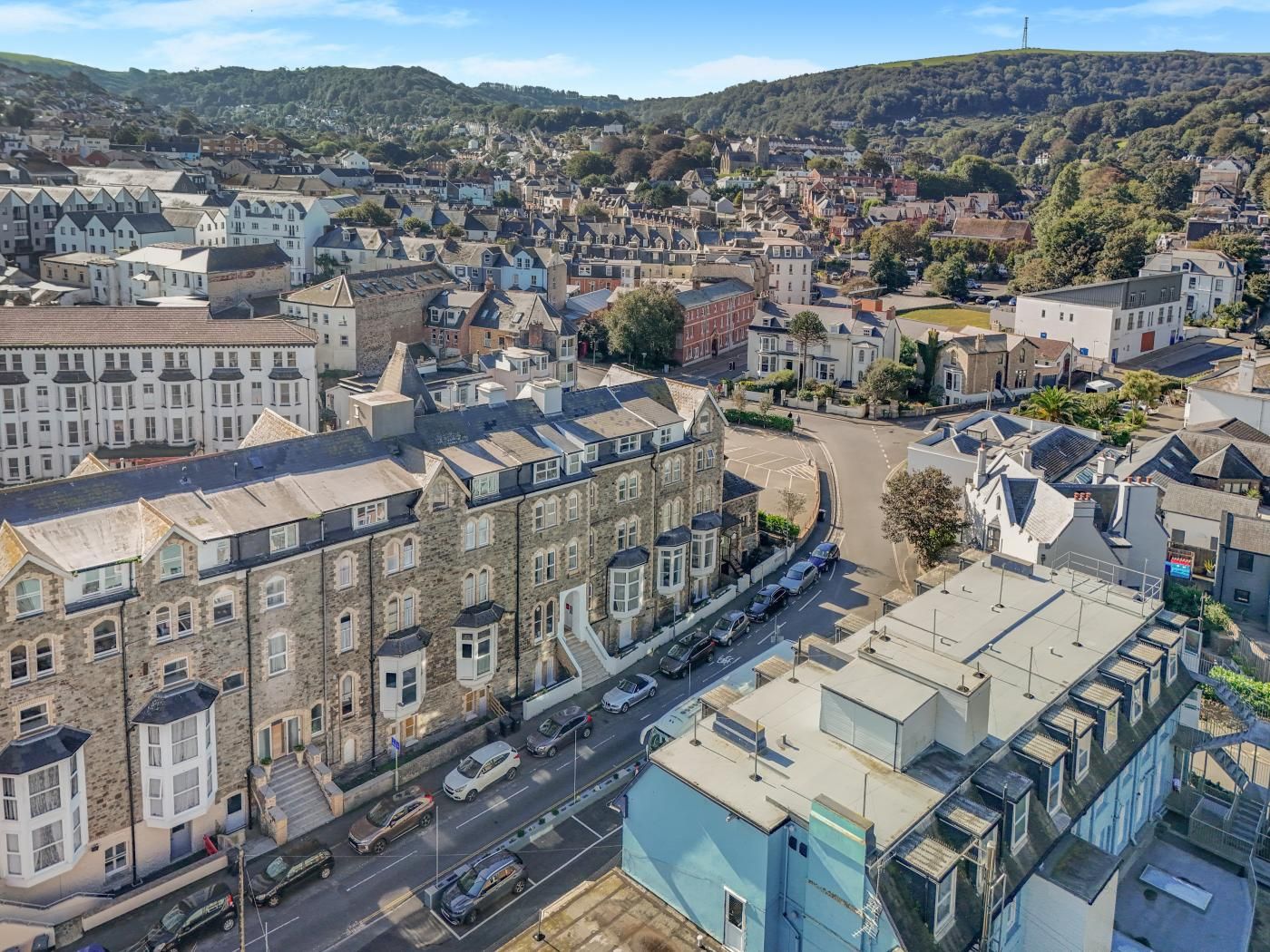 A town with a mix of residential and commercial buildings, a main road, and a hilly backdrop.