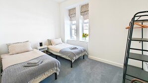 A room with two beds, a radiator, a window with curtains, and a metal shelf. - 2 Bed in Ilfracombe (oc-b45841) (Ilfracombe)