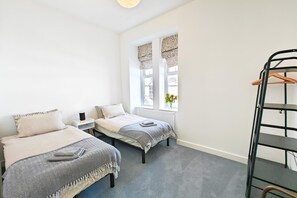 Ein Zimmer mit zwei Betten, einem Heizkörper, einem Fenster mit Vorhängen und einem Metallregal.
