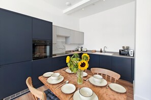 Eine moderne Küche mit dunklen Schränken, einem Einbauofen und einem Essbereich mit einem Holztisch, gedeckt für vier Personen.