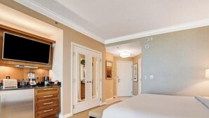 Quarto de hotel com cama, televisão, escrivaninha com cafeteira e banheiro visível através de uma porta.