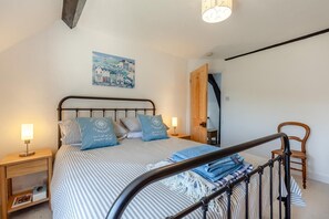 Ein Schlafzimmer mit Bett, Nachttischlampen, einem Holzstuhl, einem Bild an der Wand und einer Tür zu einem anderen Raum.