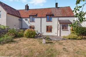 A two-story house with a red-tiled roof, a small garden with a table and chairs, and a stone pathway leading to the entrance. - 2 Bed in Cheddar (oc-v45773) (Cheddar)