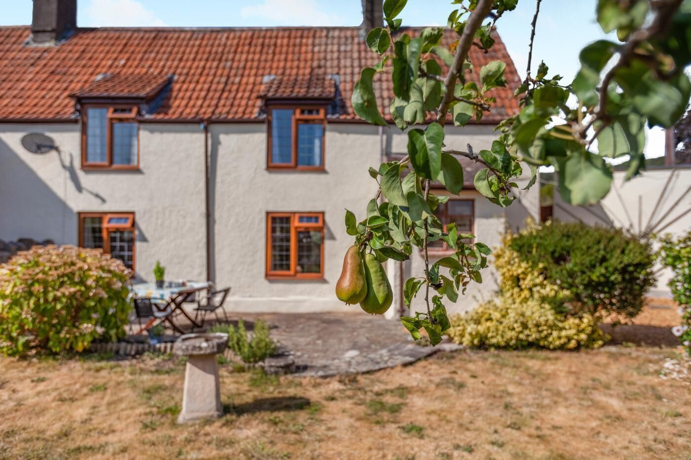 Ein Gebäude mit einem Ziegeldach, einer Terrasse mit Tisch und Stühlen und hängenden Früchten.