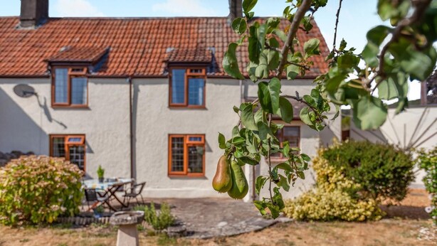 A building with a tiled roof, a patio area with a table and chairs, and a hanging fruit. - 2 Bed in Cheddar (oc-v45773) (Cheddar)