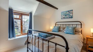 A bedroom with a bed, a window with curtains, a painting on the wall, and a nightstand with a lamp. - 2 Bed in Cheddar (oc-v45773) (Cheddar)