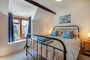 A bedroom with a bed, a window with curtains, a painting on the wall, and a nightstand with a lamp. - 2 Bed in Cheddar (oc-v45773) (Cheddar)