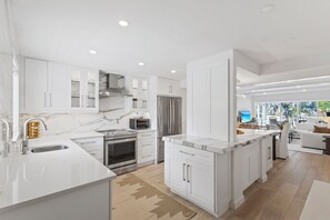 A modern kitchen with white cabinetry, a marble countertop, and stainless steel appliances. - Old Naples - Interior Designers Condo, 2 blocks from 5th Ave S & Beach! (Naples)
