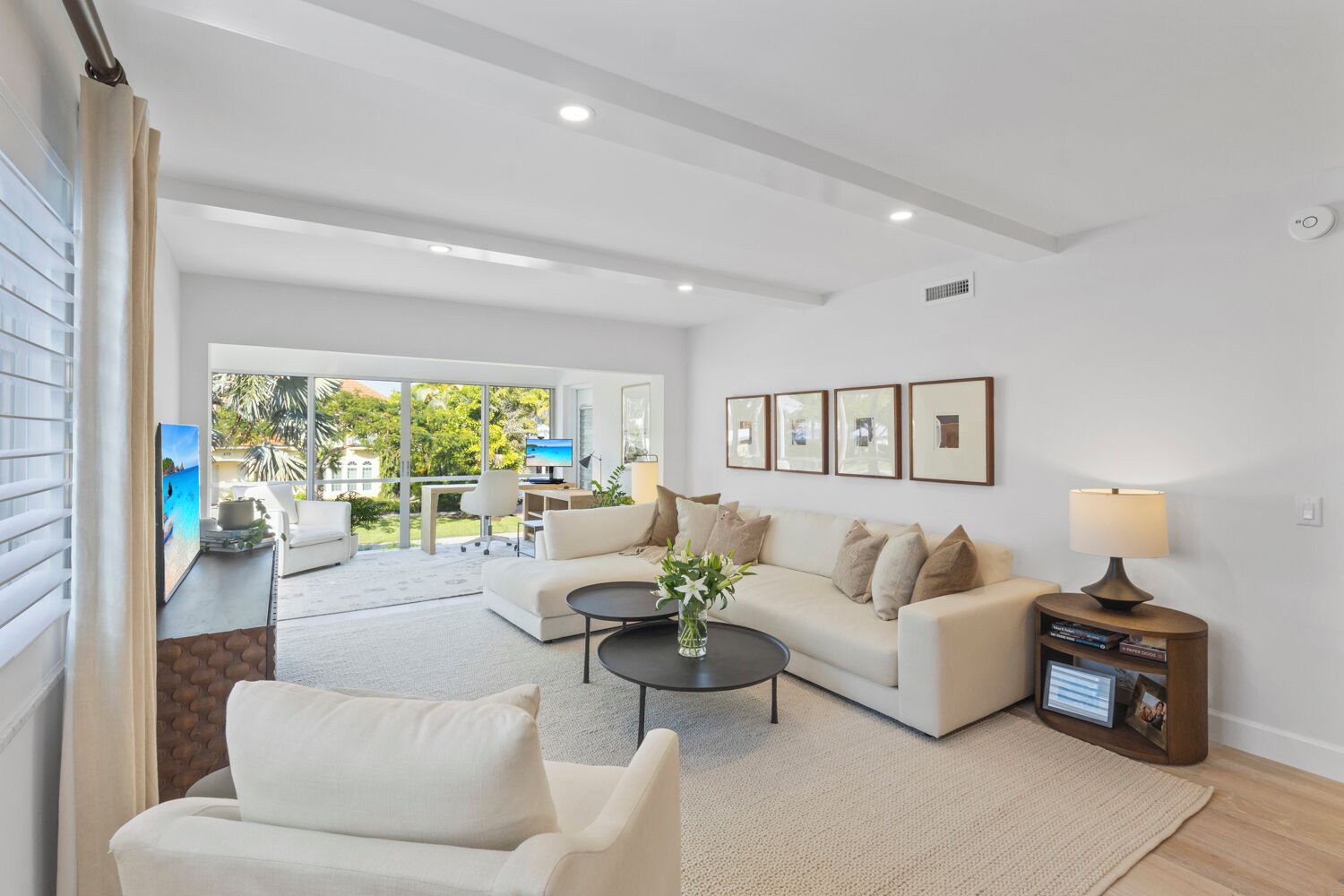 A modern living room with a sofa, coffee table, and a TV. There is a dining area with a table and chairs, and a view of the outdoors.