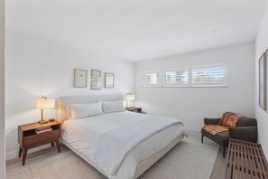 Ein Schlafzimmer mit einem großen Bett, Nachttischen, einem Sessel und einem Fenster mit Jalousien.