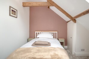 Quarto com uma cama de solteiro, cabeceira de madeira, duas mesas de cabeceira e uma porta.